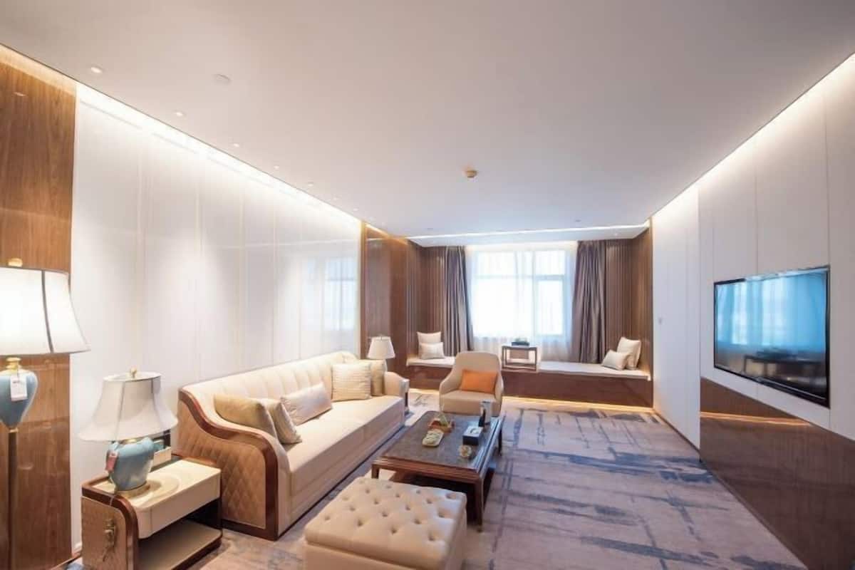 A modern hotel room with a sofa, armchair, ottoman, coffee table, and a flat-screen TV.
