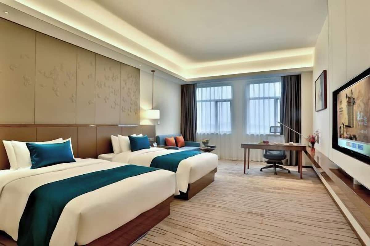 A hotel room with two beds, a desk, and a large window.