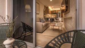 A modern living room with a sofa, coffee table, and chairs, leading to a kitchen area with a TV and modern appliances. - Houze Residences – By AVA Rentals. (Asunción)