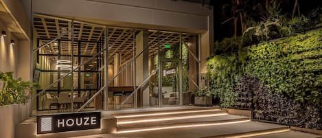 A modern building with a glass entrance, outdoor seating, and a sign reading "HOUSE".