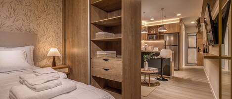 Ein modernes Schlafzimmer mit einem großen Bett, einem Holzschrank und einer kleinen Küchenzeile im Hintergrund.
