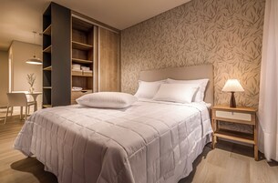 Ein ordentlich bezogenes Bett mit Kopfteil, ein Nachttisch mit Lampe und ein Kleiderschrank mit Regalen.