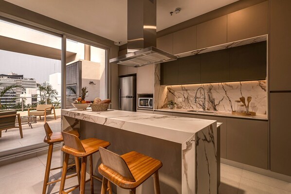 Una cocina moderna con encimera de mármol, electrodomésticos de acero inoxidable y taburetes de madera.