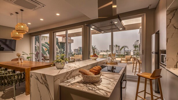 A modern kitchen with a marble countertop, wooden chairs, and a large window overlooking a cityscape. - Houze Residences – By AVA Rentals. (Asunción)