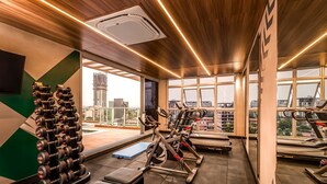 A gym with exercise equipment, a large mirror, and a view of the city. - Houze Residences – By AVA Rentals. (Asunción)