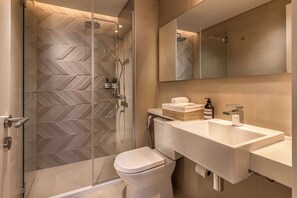 A modern bathroom with a glass-enclosed shower, a white toilet, and a large sink with a mirror above it. - Houze Residences – By AVA Rentals. (Asunción)