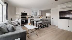 Una sala de estar moderna con un sofá gris, una mesa de centro blanca y un comedor con una mesa y bancos.