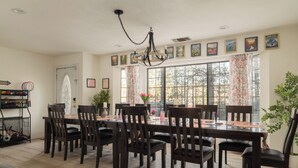 Un comedor con una mesa larga, varias sillas, una araña y ventanas grandes con cortinas.