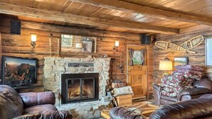 Un acogedor interior de cabaña de madera con chimenea de piedra, sofás de cuero y decoración rústica.