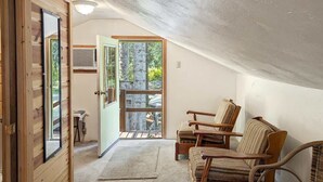 Una habitación acogedora con paredes de madera, un ventanal y vistas a árboles. Hay dos sillas de madera y una mesita.