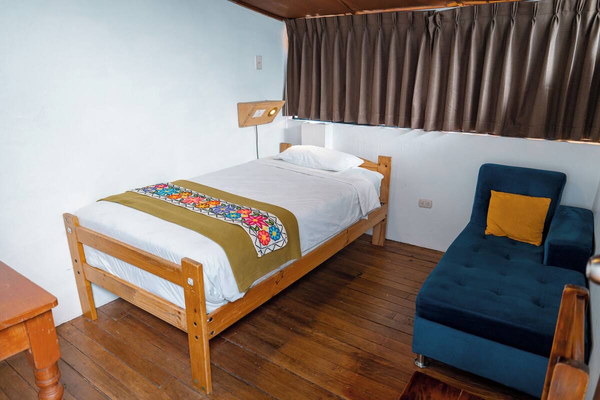Una cama individual con estructura de madera, colcha colorida y mesita de noche.