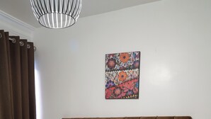 Una cama bien hecha con una colcha estampada, dos almohadones decorativos y una obra de arte colgada en la pared.