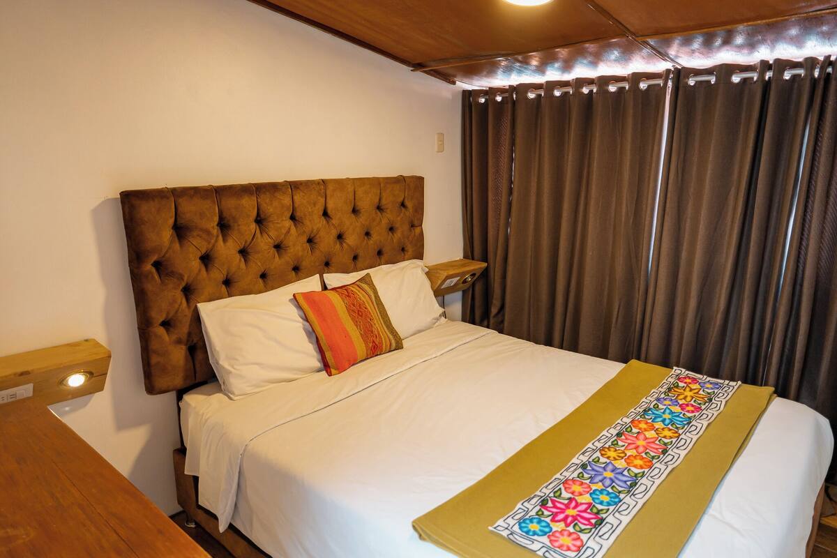 Una cama bien hecha con un cabecero capitonado, ropa de cama blanca y una colcha bordada de colores.