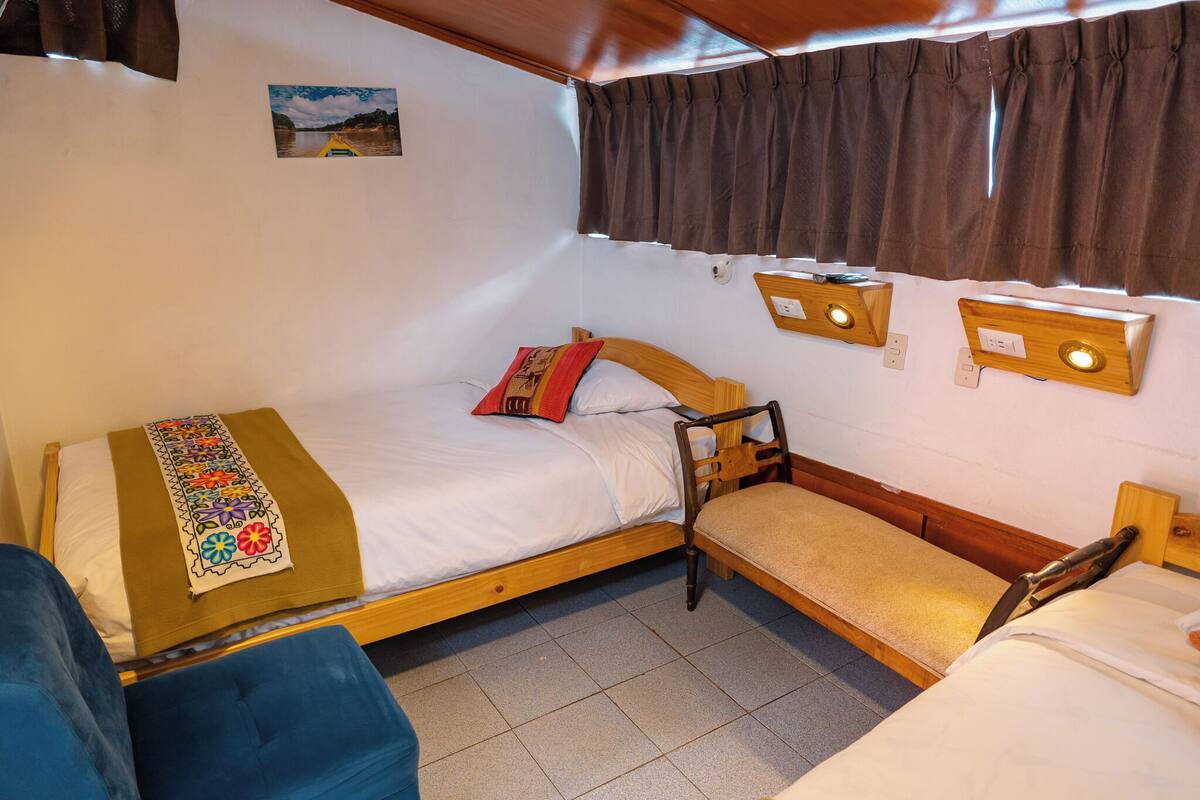Una habitación pequeña y acogedora con una cama individual, un banco y una mesita con una radio.
