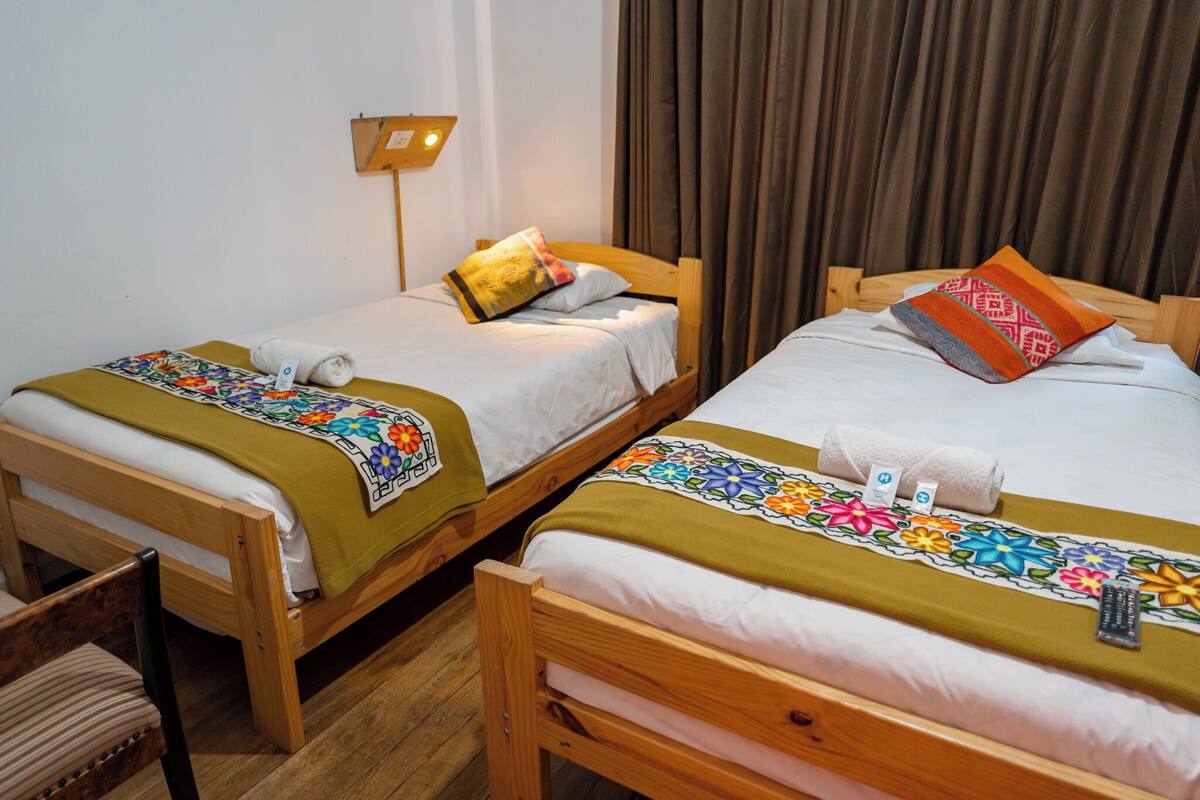Dos camas de madera con sábanas blancas y colchas florales de colores.