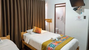 Habitación de hotel con cama, escritorio, silla, lámpara de escritorio, televisión montada en la pared y puerta de baño.