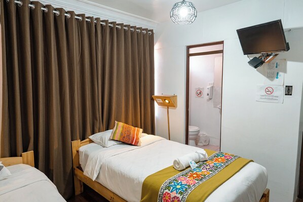 Habitación de hotel con cama, escritorio, silla, lámpara de escritorio, televisión montada en la pared y puerta de baño.