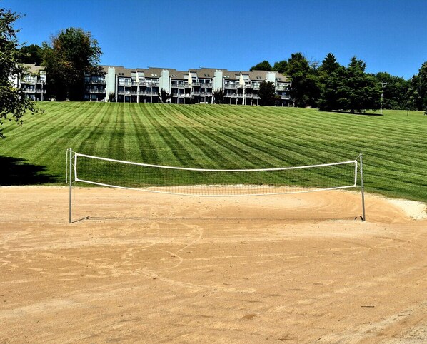 A tennis court with a net, surrounded by a well-maintained lawn and a building in the background.