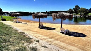 Una playa con sombrillas de paja y sillas reclinables frente a un lago tranquilo.
