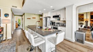 Una cocina moderna con armarios blancos, una isla central con taburetes y electrodomésticos de acero inoxidable, y vistas al comedor.