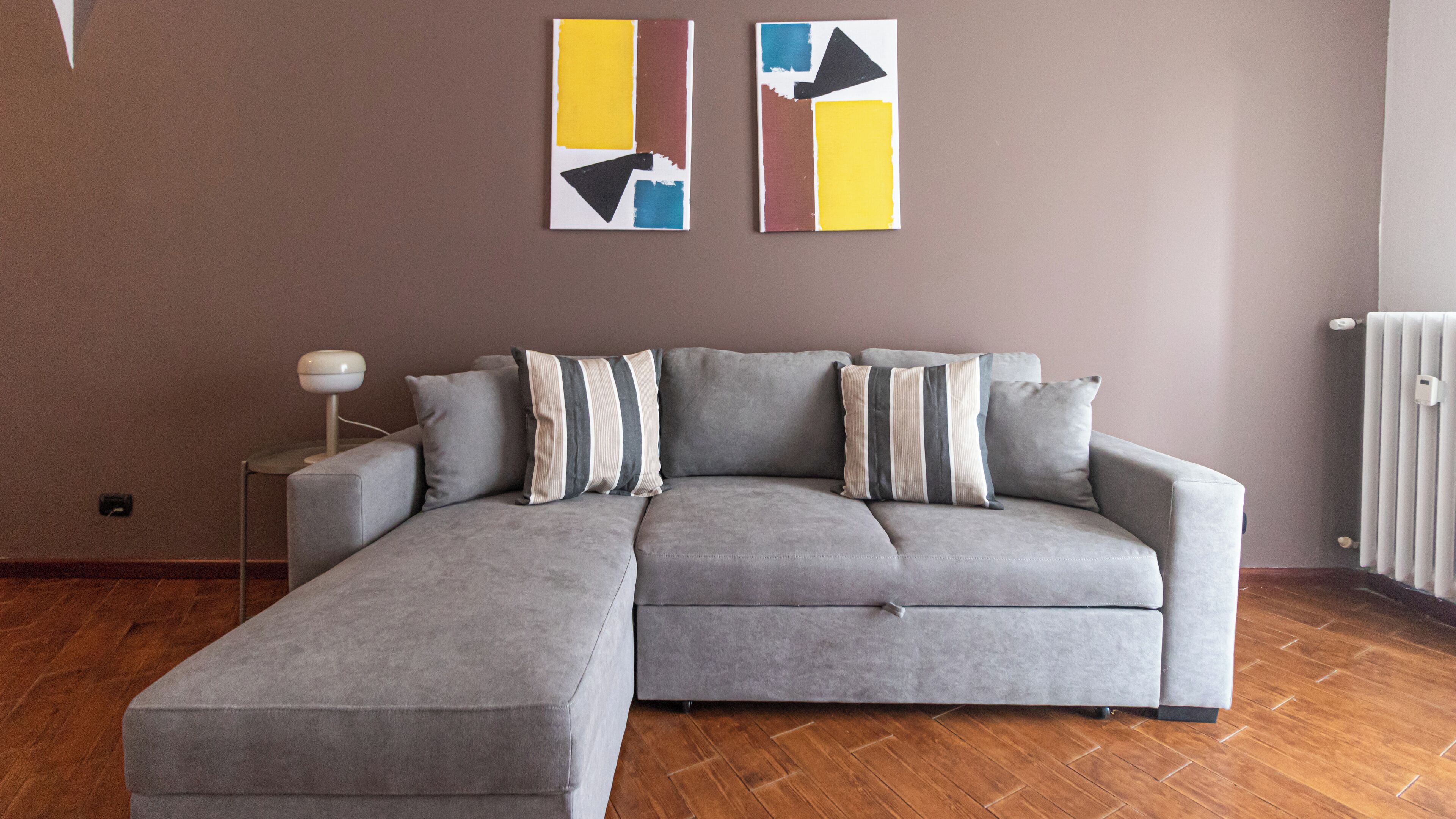 Un canapé d’angle gris avec des coussins à rayures, un lampadaire et une œuvre d’art abstraite accrochée au mur.