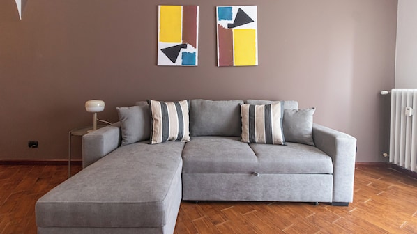 A grey sectional sofa with striped pillows, a floor lamp, and abstract art on the wall.