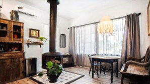 A cozy living room with a wooden floor, a fireplace, a dining table with chairs, and a large window with curtains. - Rustic Studio Rain Shower 3min-asian Dist (Oklahoma City)