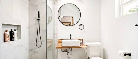 A modern bathroom with a glass-enclosed shower, a round mirror, a sink with a wooden countertop, and a toilet.