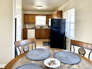 Una cocina con armarios de madera, un refrigerador negro, un lavavajillas blanco y una mesa de comedor con individuales y un plato de comida.