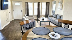 Ein Wohnzimmer mit einer Couch, Sesseln, einem Couchtisch und einem an der Wand montierten Fernseher.