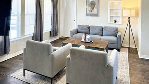 Ein Wohnzimmer mit grauem Sofa, zwei Sesseln, einem Holztisch und einer Stehlampe.