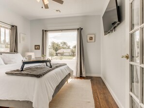 A bedroom with a bed, bedside table, lamp, and a window with curtains. - 2BR Stylish Retreat in Midtown (Oklahoma City)