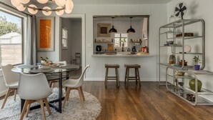 Una cocina moderna con una isla central, luces colgantes y una zona de comedor con una mesa redonda y sillas.
