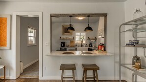 Una cocina moderna con una isla central, iluminación colgante y una estantería metálica.
