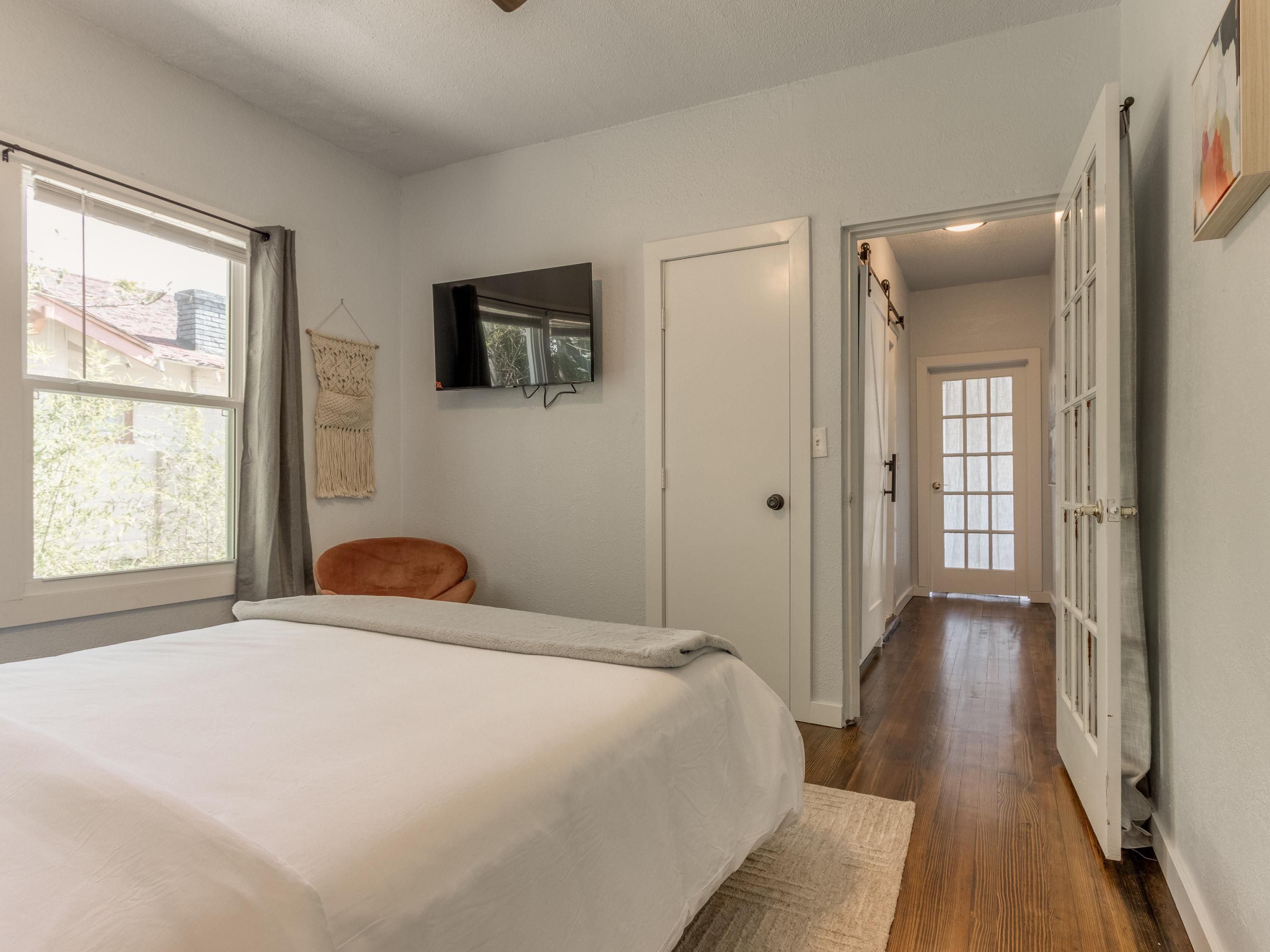 A bedroom with a large bed, a TV mounted on the wall, and a door leading to a hallway.