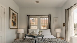 Una habitación de hotel con una cama, dos mesitas de noche, una ventana con cortinas y obras de arte en las paredes.