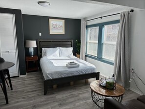 A neatly arranged bedroom with a bed, bedside table, lamp, and a small round table with toiletries. - Cute Tiny House With Fenced Yard Near Plaza Dist (Oklahoma City)