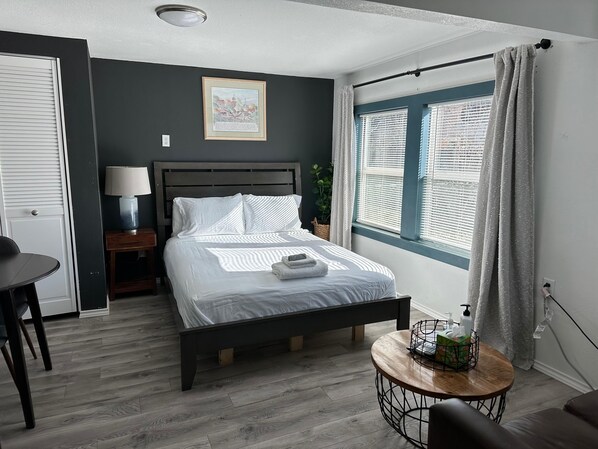 A neatly arranged bedroom with a bed, bedside table, lamp, and a small round table with toiletries. - Cute Tiny House With Fenced Yard Near Plaza Dist (Oklahoma City)