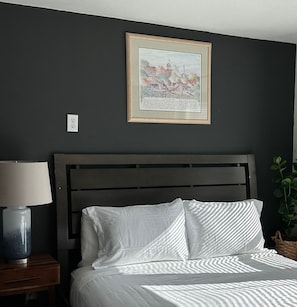 A bedroom with a bed, a nightstand, a lamp, a framed picture on the wall, and a plant. - Cute Tiny House With Fenced Yard Near Plaza Dist (Oklahoma City)