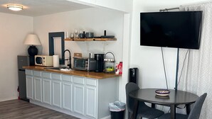 A compact kitchen with a microwave, toaster, and coffee maker, a small dining table with chairs, and a TV mounted on the wall.