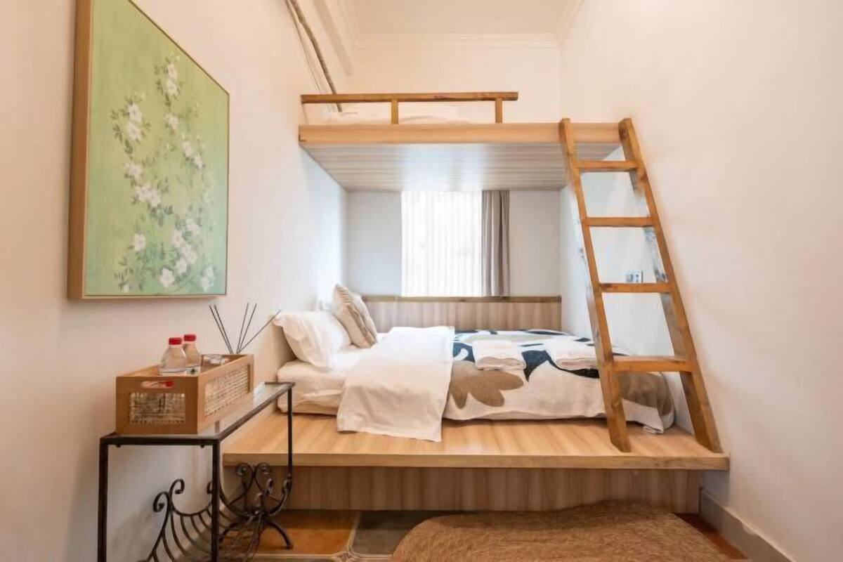 A bunk bed with a ladder, a bedside table with a radio, and a painting on the wall.