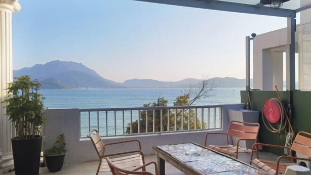 Een balkon met een tafel en stoelen, met uitzicht op een waterpartij en bergen.