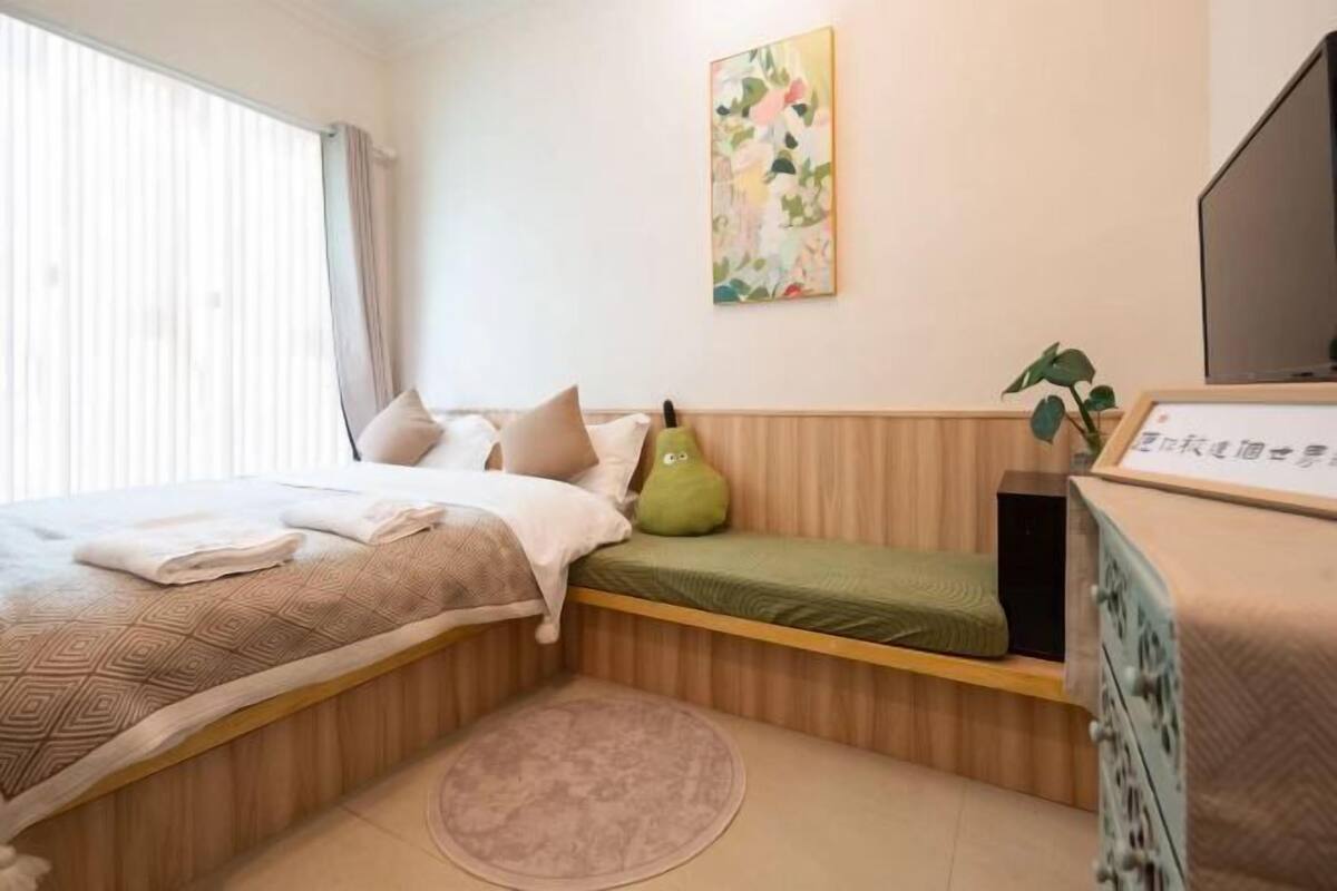 A bedroom with a bed, a small bench, a television, and a plant.