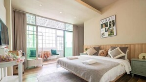 Een moderne hotelkamer met een groot bed, een bureau met stoel, een klein tafeltje met bloemen en een groot raam met gordijnen.