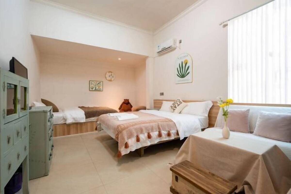A hotel room with two beds, a wooden chest of drawers, a clock, and a wall-mounted air conditioner.