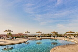 A pool area with lounge chairs and umbrellas, surrounded by a low wall and palm trees. - One Bedroom Residence Los Cabos (Cabo San Lucas)