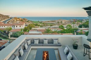 A rooftop terrace with a fire pit, outdoor seating, and a view of the ocean and coastal buildings. - One Bedroom Residence Los Cabos (Cabo San Lucas)