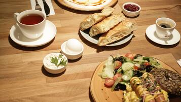 A wooden table with various breakfast items including bread, a hot dog, a salad, and two cups of coffee.