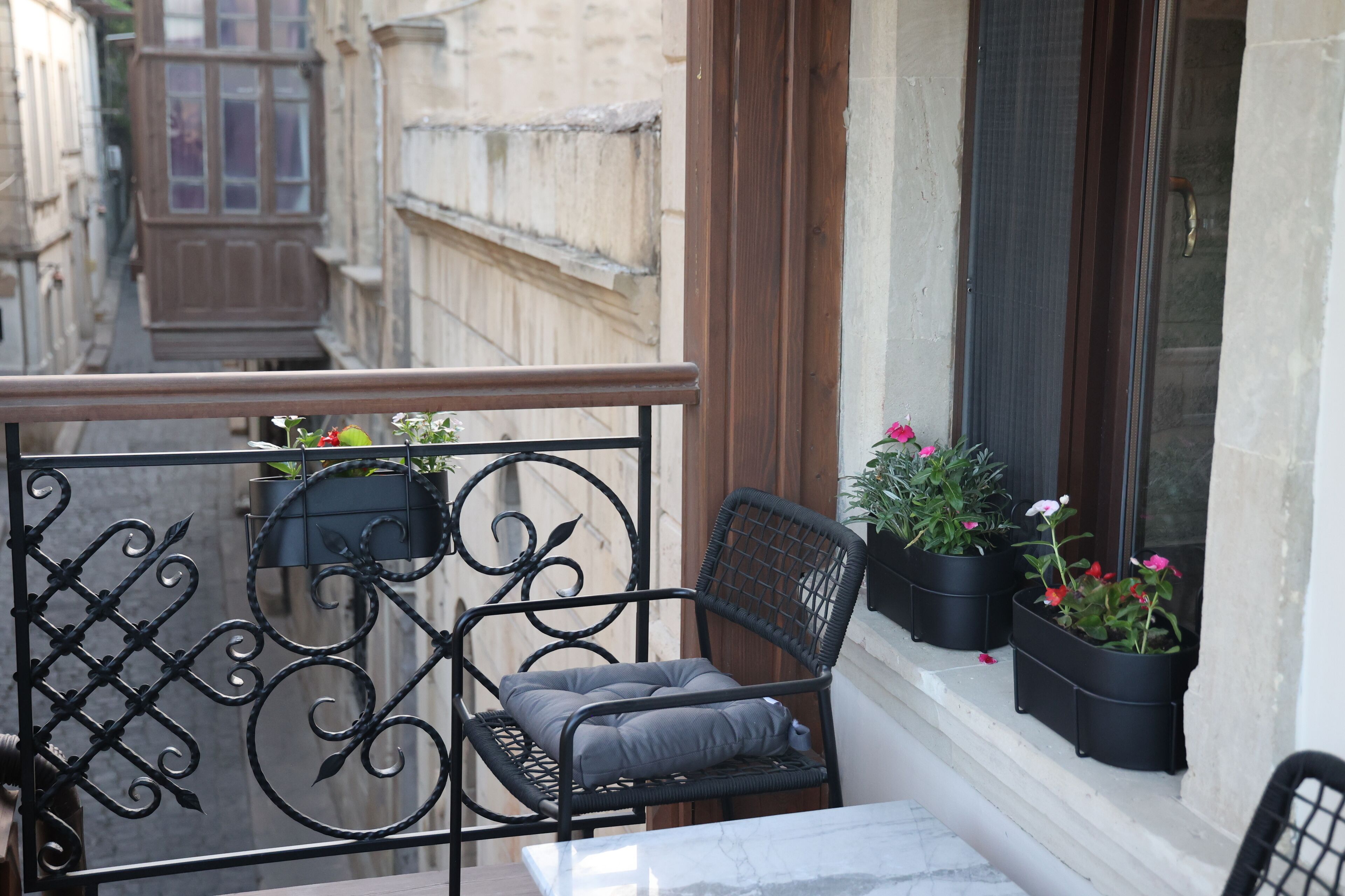 A balcony with a metal railing, a cushioned chair, a table, and potted plants.