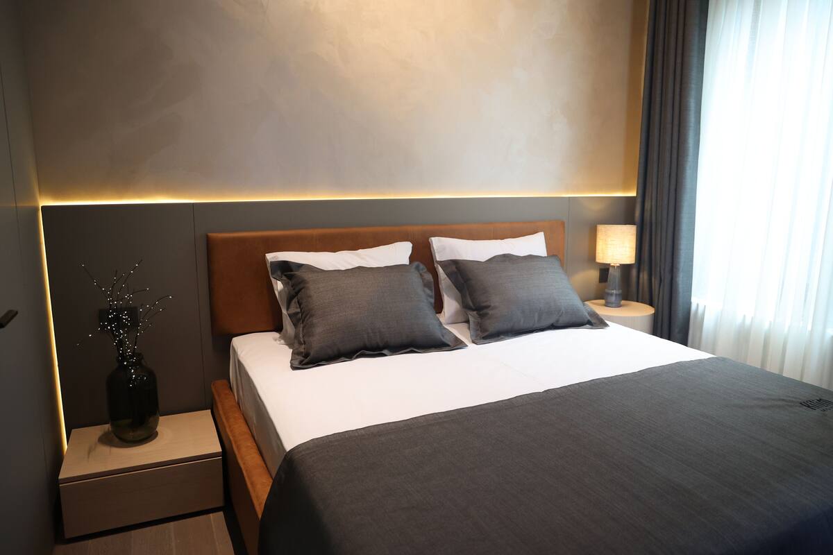 Ein modernes Hotelzimmer mit einem großen Bett, einem Nachttisch, einer Lampe und einer Vase mit Zweigen.